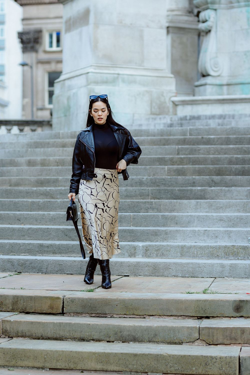 Stylish winter outfit featuring a black sweater, snake print pencil skirt and boots on stone steps of a classic building.