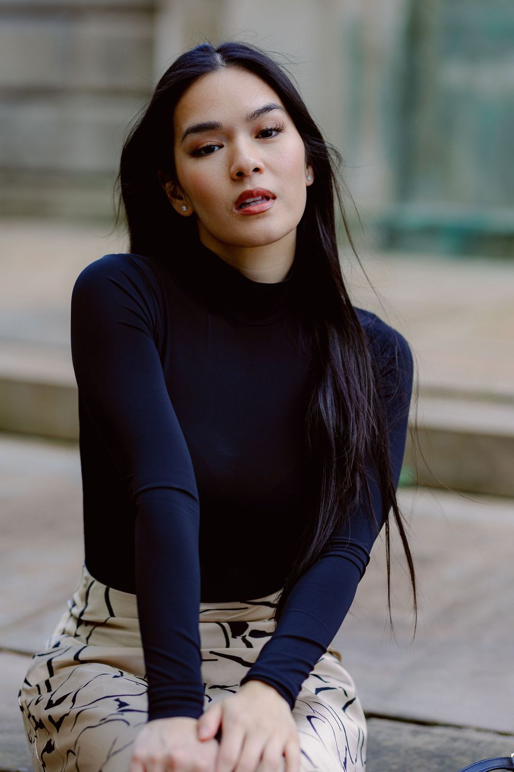 Woman in navy turtleneck sweater poses elegantly against blurred architectural background.