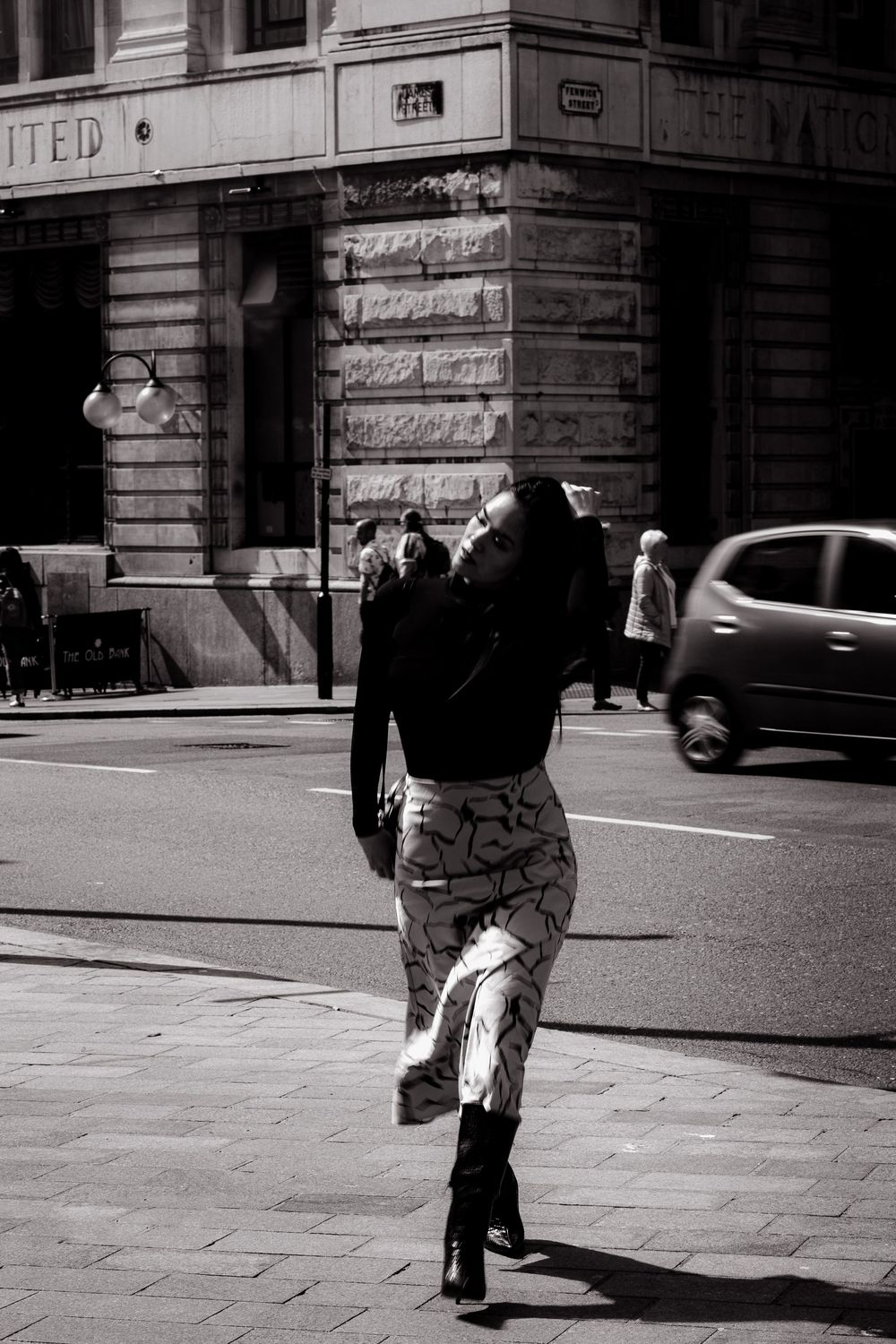 Black and white street photography sequence shows a person walking past a building corner in an urban setting.