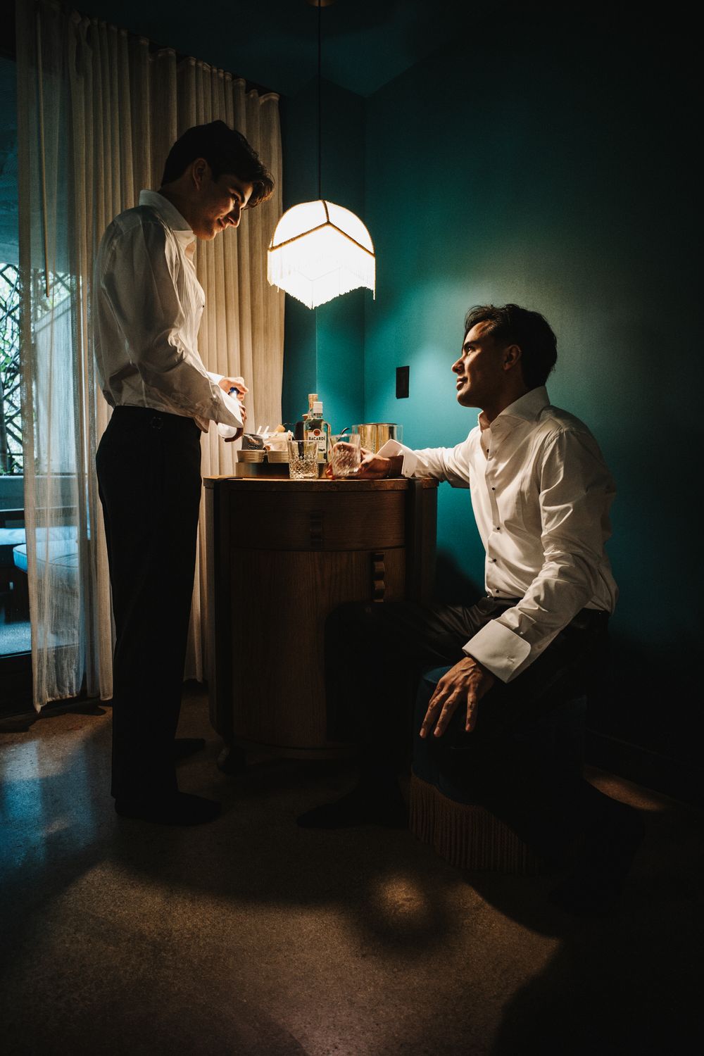 Two people in white shirts interact in a moody room with dramatic lighting and teal walls.