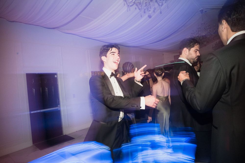 Men in tuxedos dancing at an elegant formal event with blue ambient lighting on the dance floor.