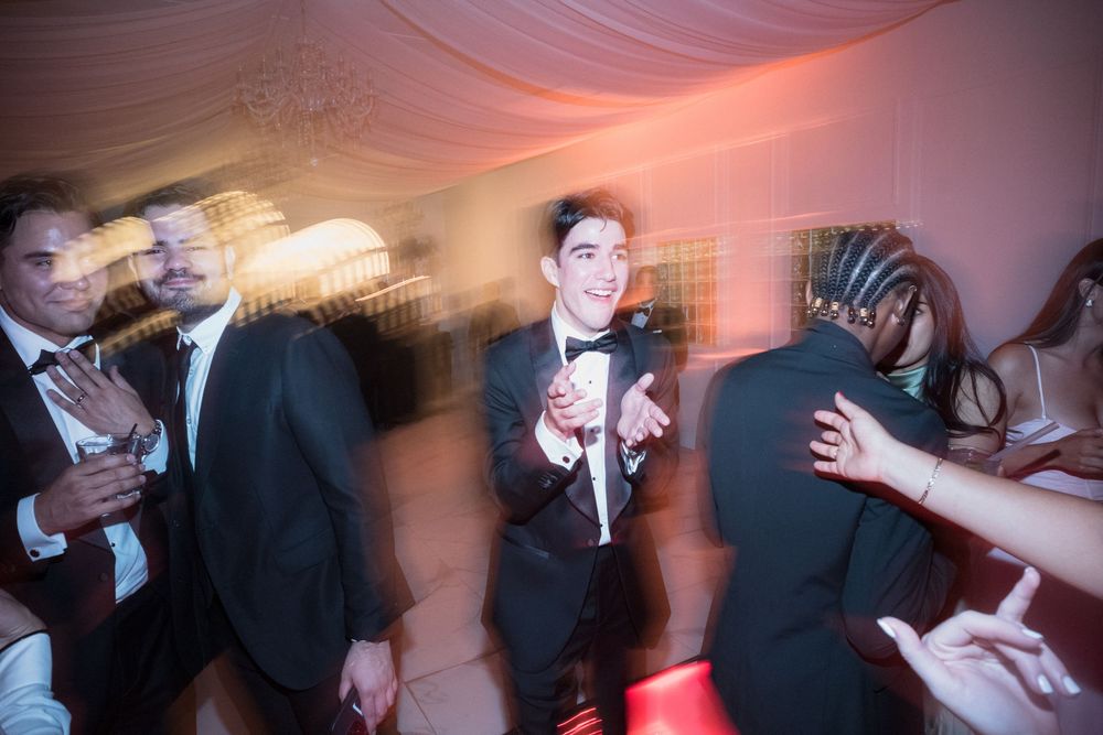Groom in black tuxedo dancing joyfully with guests at elegant wedding reception party.