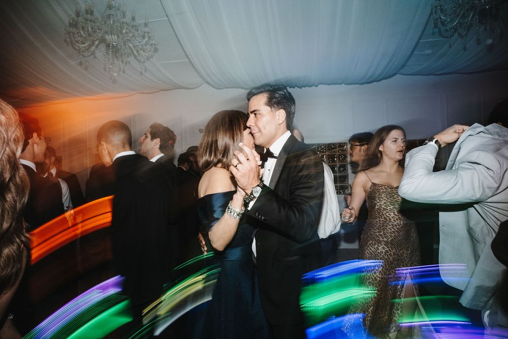 People dancing and celebrating at a nightclub with colorful light trails and motion blur effects in the background.