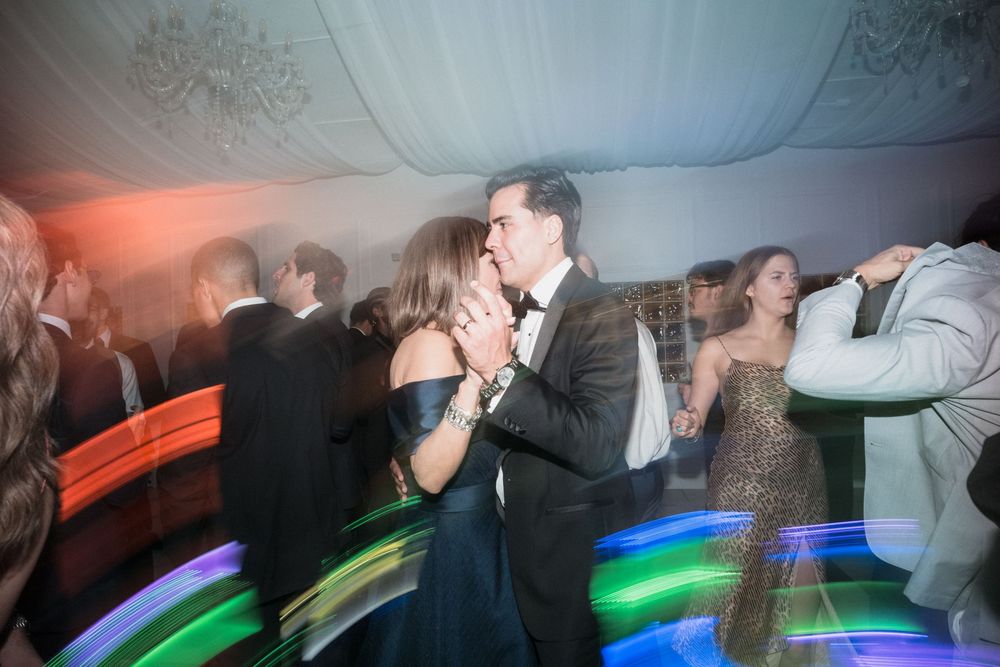 Couple sharing a romantic kiss on a lively dance floor at a formal evening gala event.