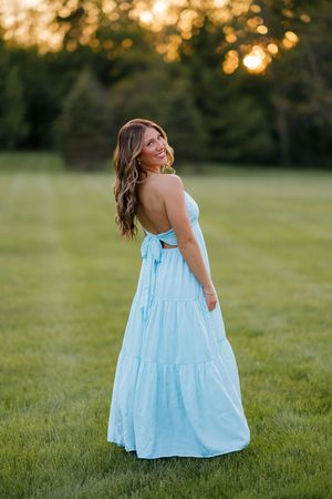 Young woman in a light blue strapless tiered maxi dress smiling over her shoulder at golden hour.
