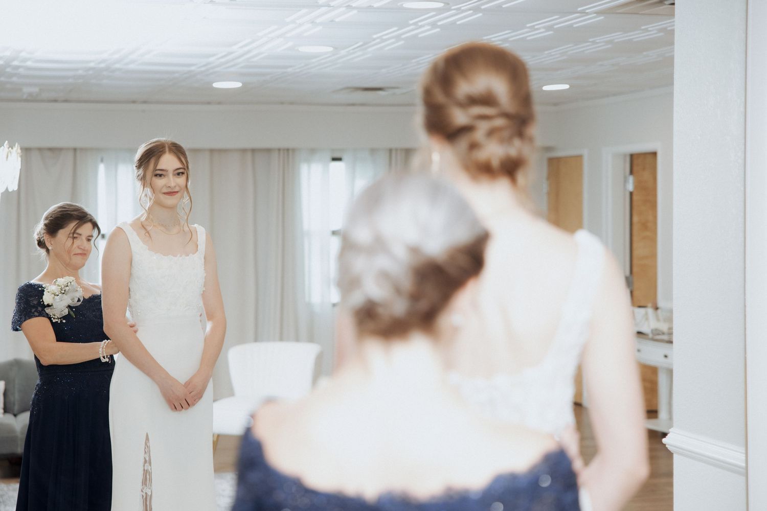 A bride in a white dress poses near a window with natural light streaming in, creating a soft, romantic atmosphere.