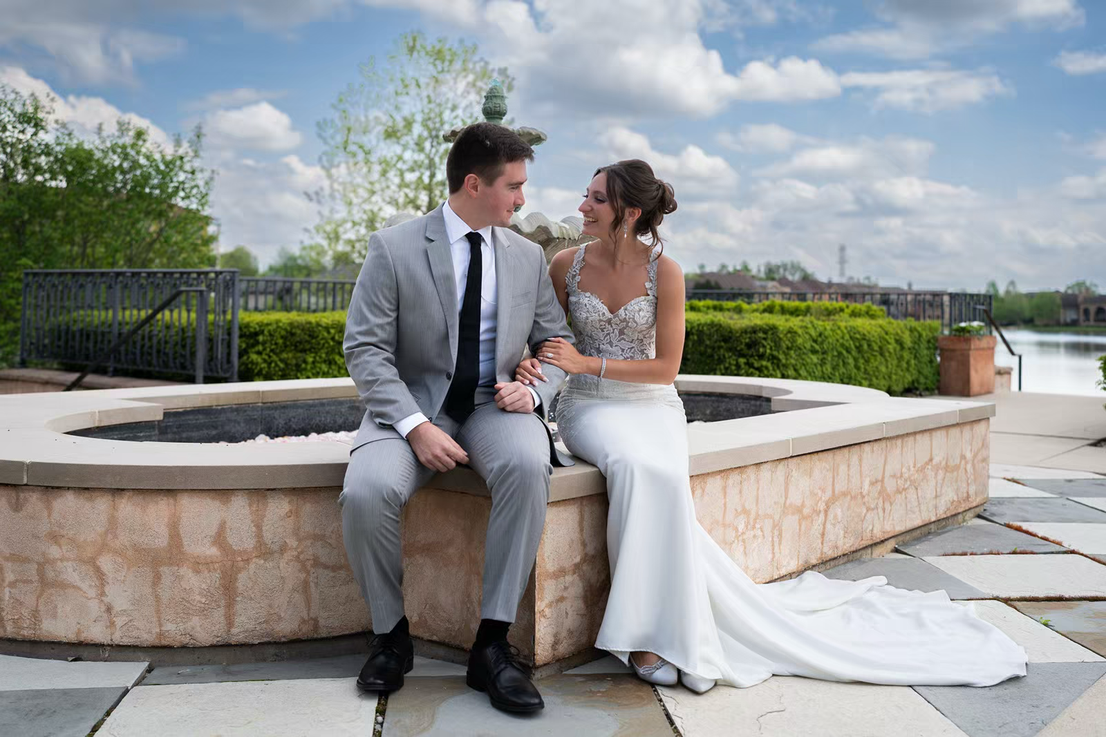 A couple sits together on a stone wall overlooking a scenic outdoor venue on their wedding day.