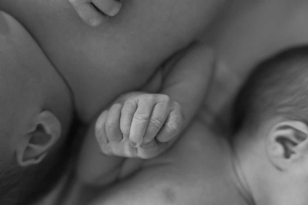 Newborn twins in the hospital. Photography ideas of capturing the special bond. Newborn twins holding hands. Black and white timeless image.