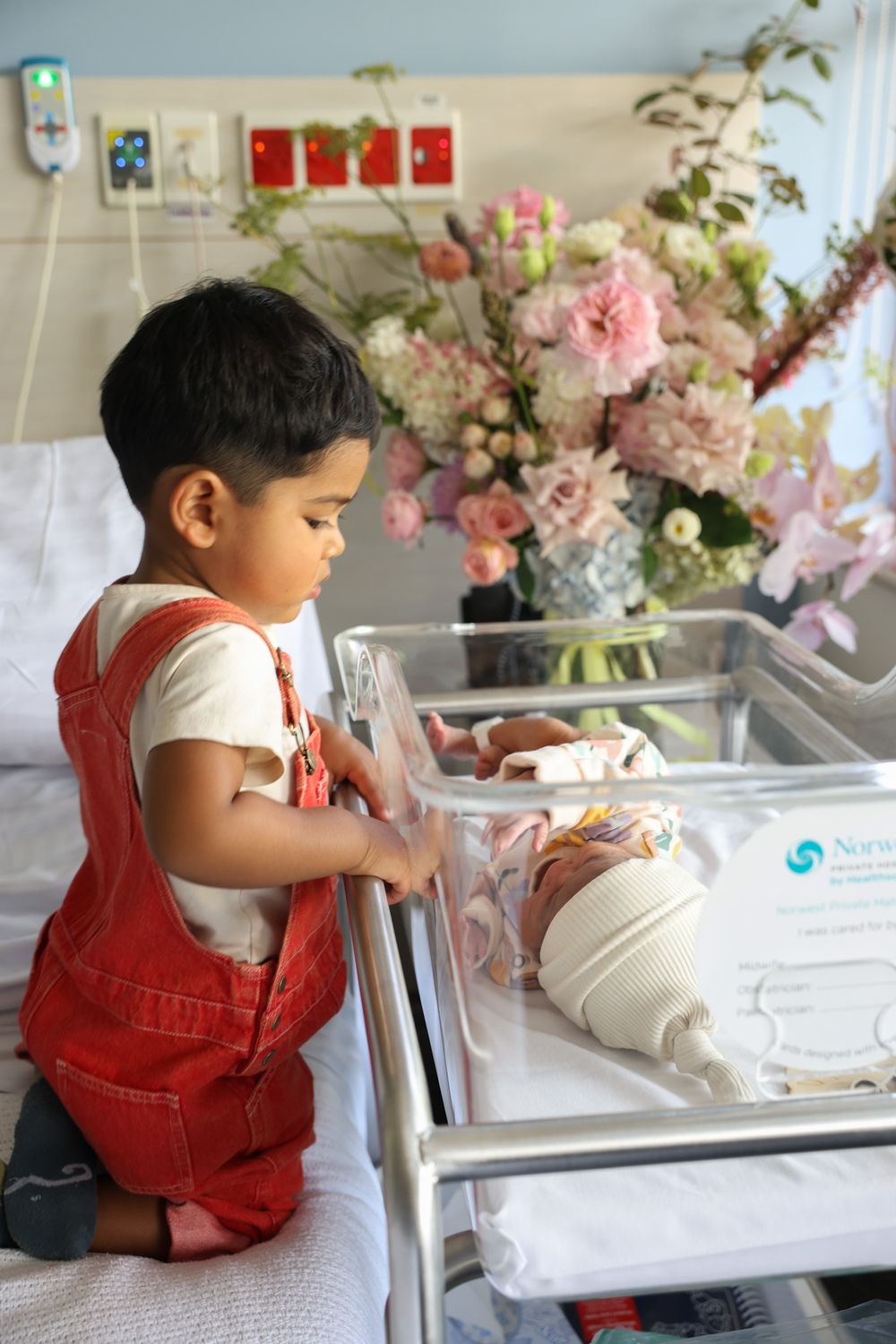 Sibling meeting his newborn sister for the first time at the hospital. Looking over into the cot to see her little face. Norwest Private.