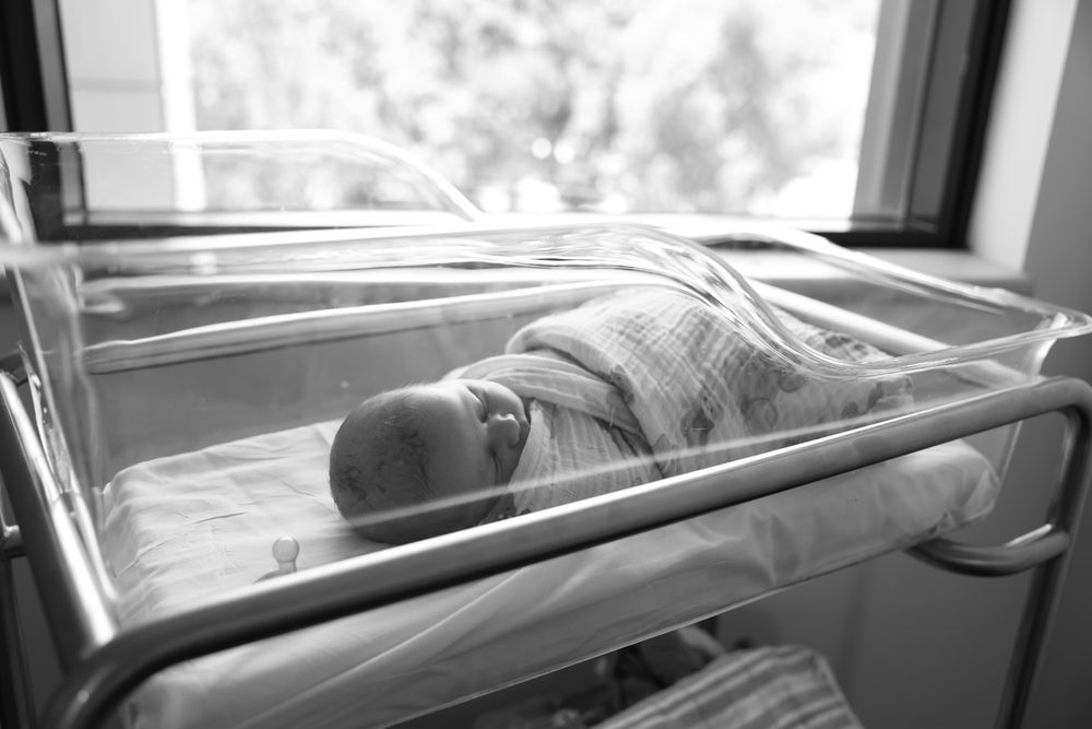 Quiet bonding moment between the parents as they look over their new baby in the hospital cot. Documentary style black and white.