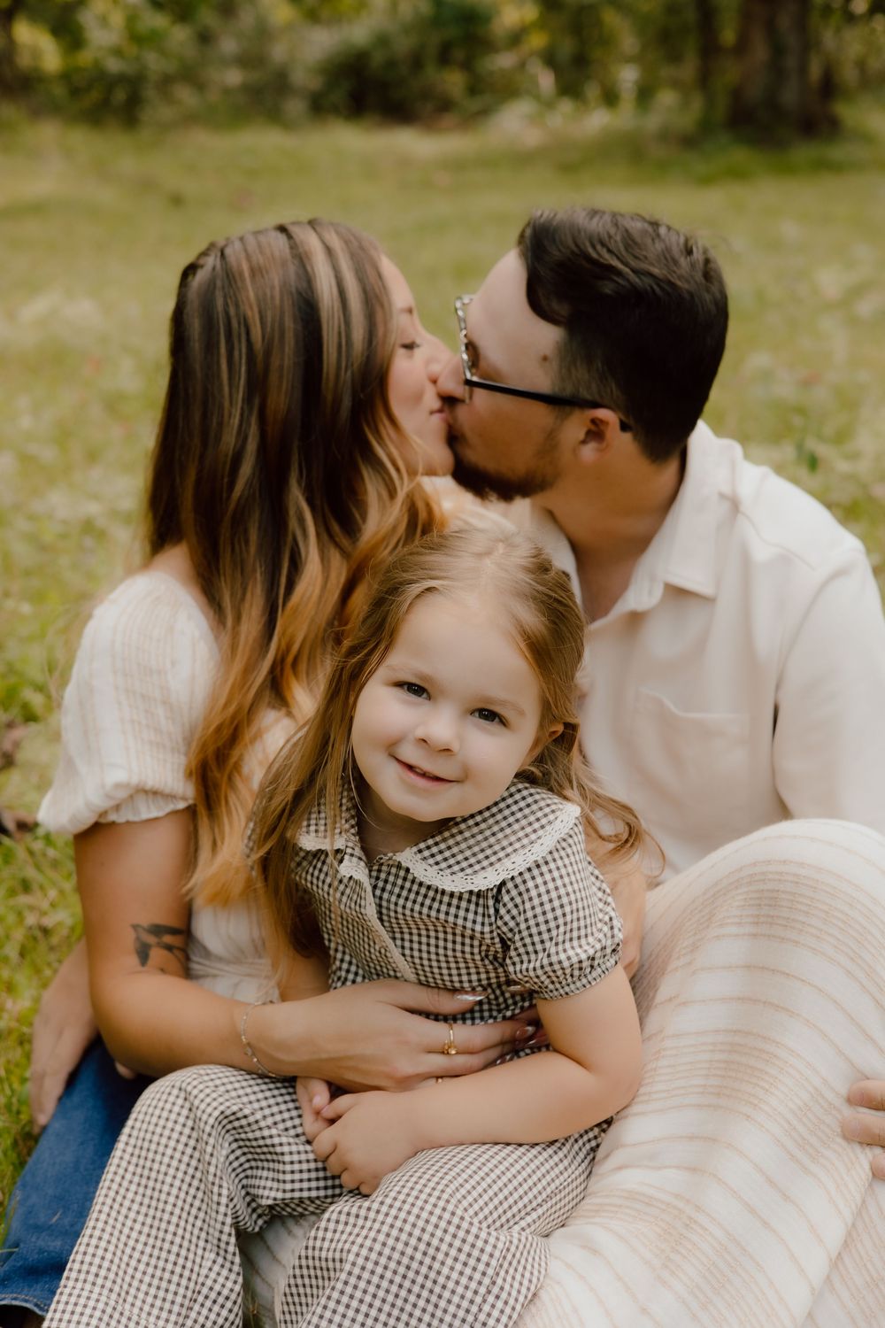 A family shares tender moments outdoors in a series of intimate portraits wearing white and gingham outfits.