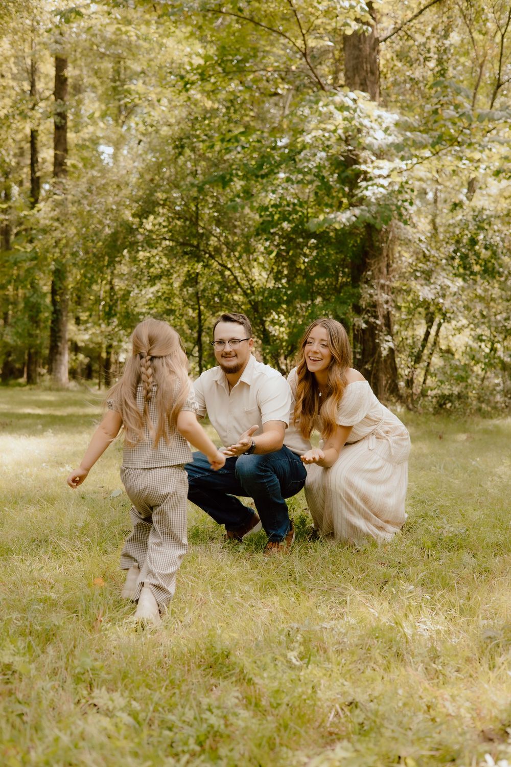 Family sitting together on grass in a sunny wooded area during an outdoor photo session.