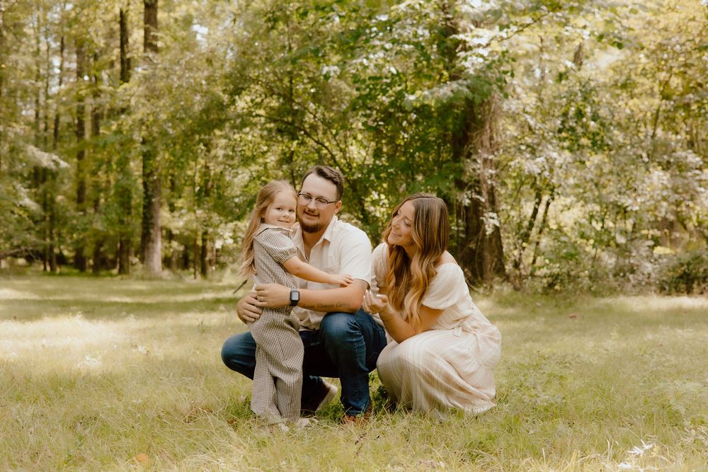 A couple shares tender moments together in a sun-dappled forest setting during an outdoor photo session.