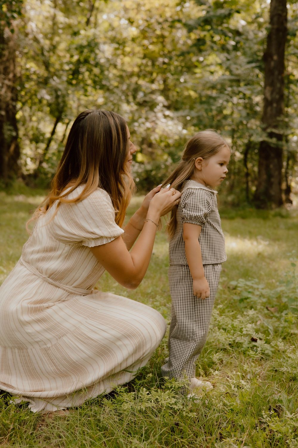 Two people in light colored dresses playing hide and seek in a sunlit forest setting.