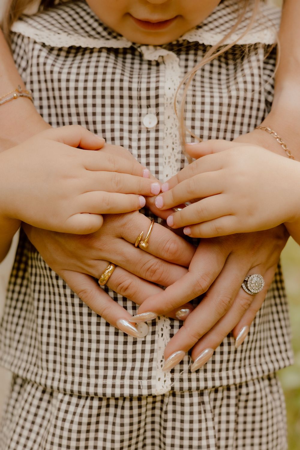 Close-up view of hands wearing wedding and engagement rings against a black and white gingham dress pattern.