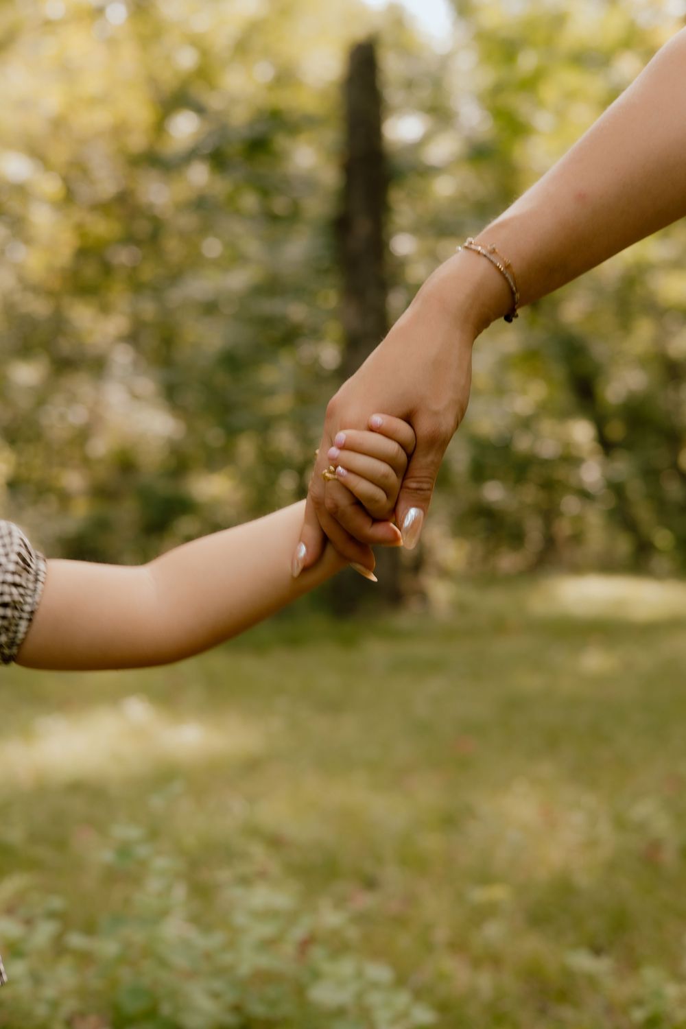 Close-up view of two hands reaching out to hold each other against a blurred natural outdoor background.