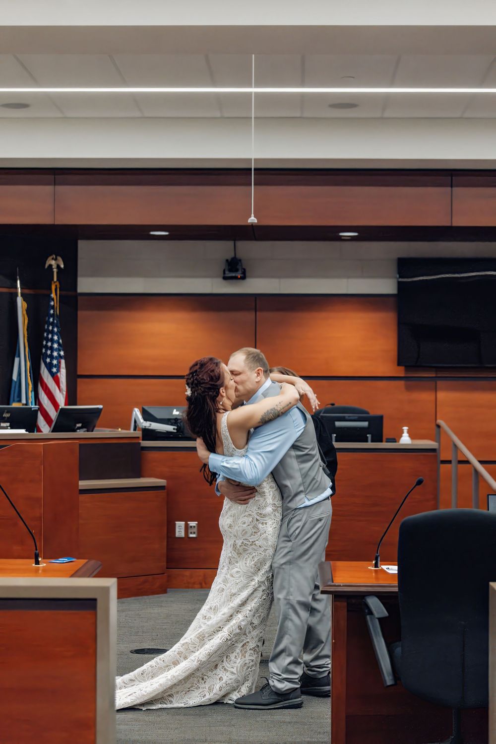 A couple shares their first kiss during an intimate courthouse wedding ceremony in front of a judge's bench.