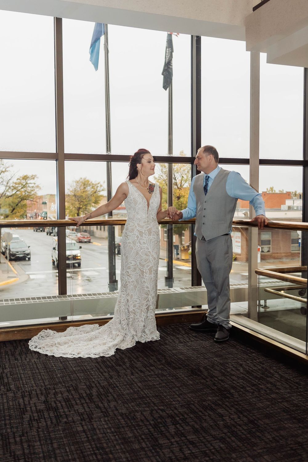 A wedding first look moment captured in a bright indoor venue with large windows and dark carpeted floors.