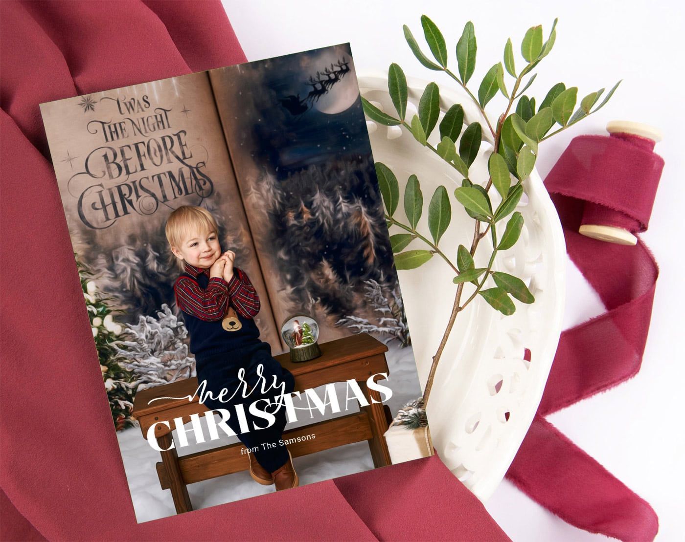 Christmas card layflat of a toddler boy with a cherubic expression dressed in a Christmas outfit in a "Night Before Christmas" scene.