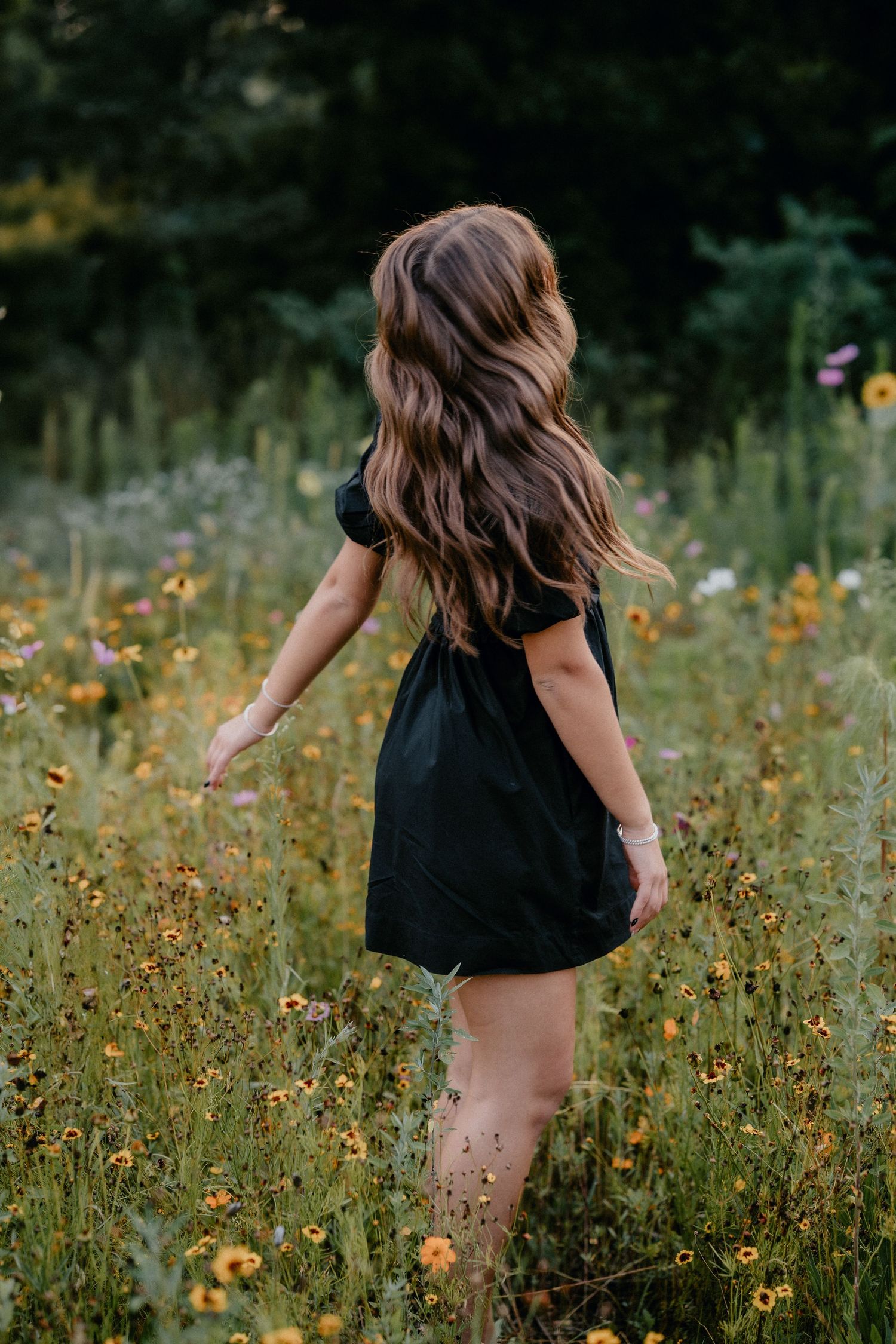 Person in a black dress twirling among wildflowers in a summer meadow.
