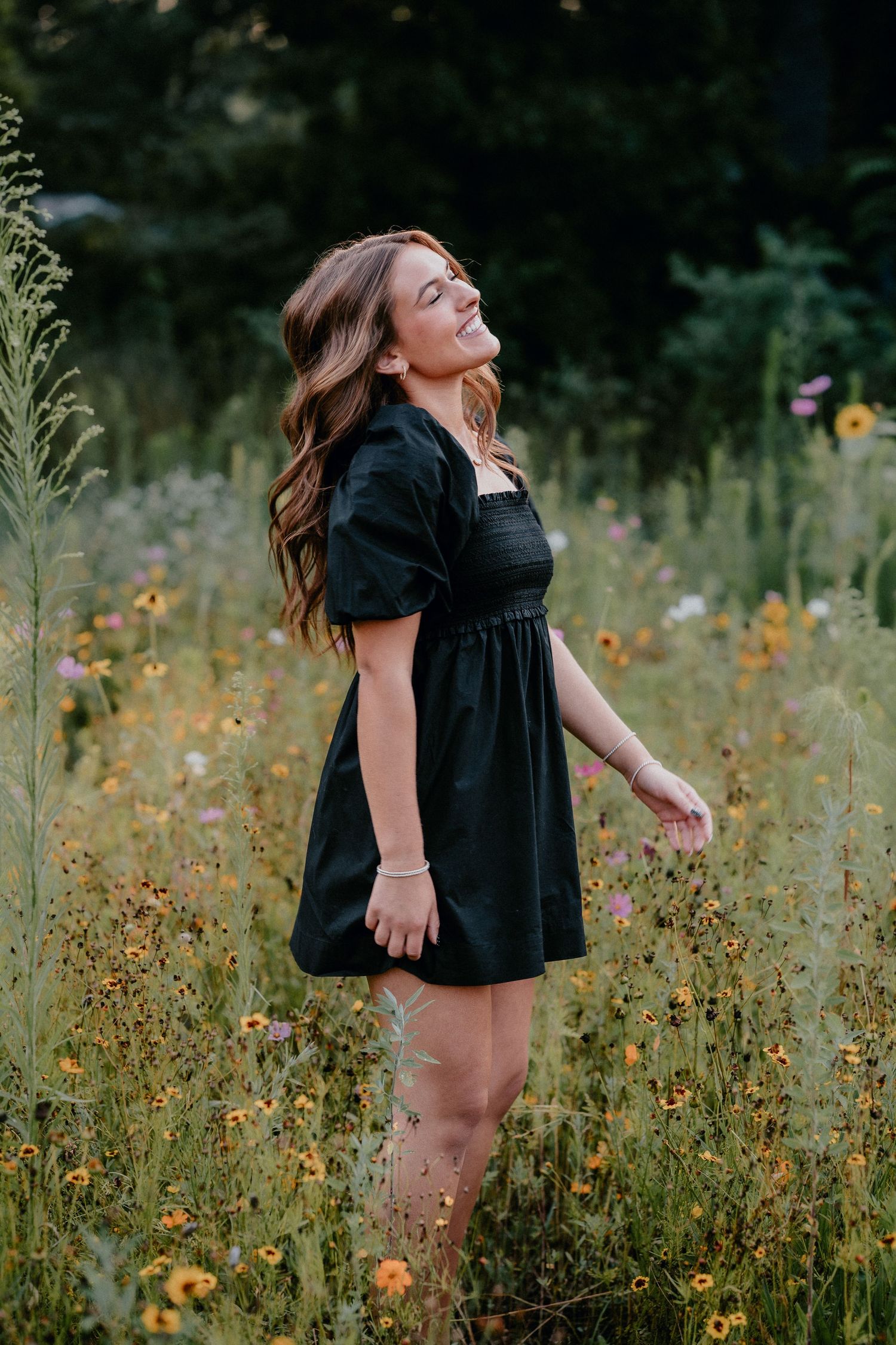 Artistic movement portrait in a black dress among wild summer flowers and tall grass.