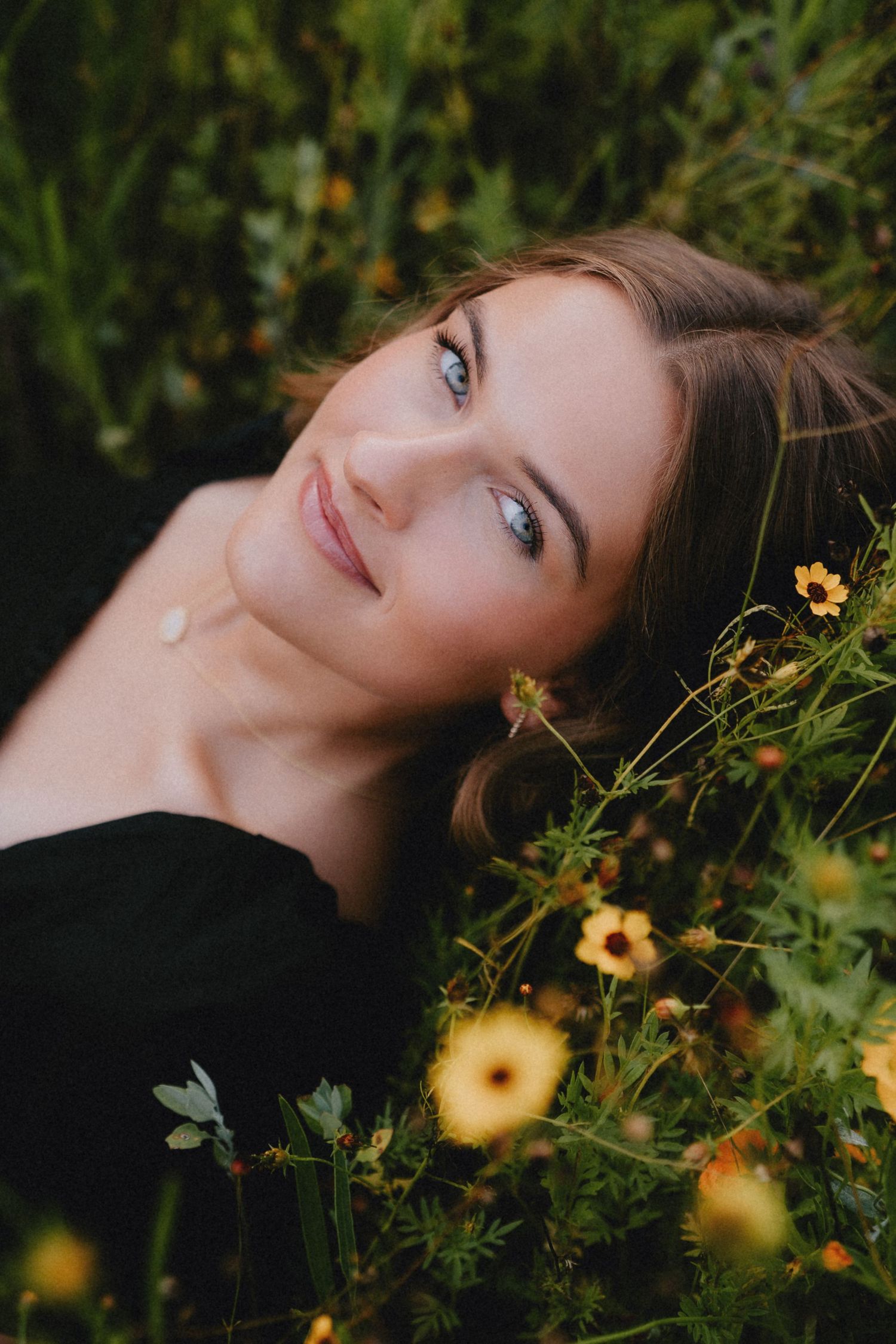 Artistic portrait in a field of yellow wildflowers against lush green foliage on an overcast day.