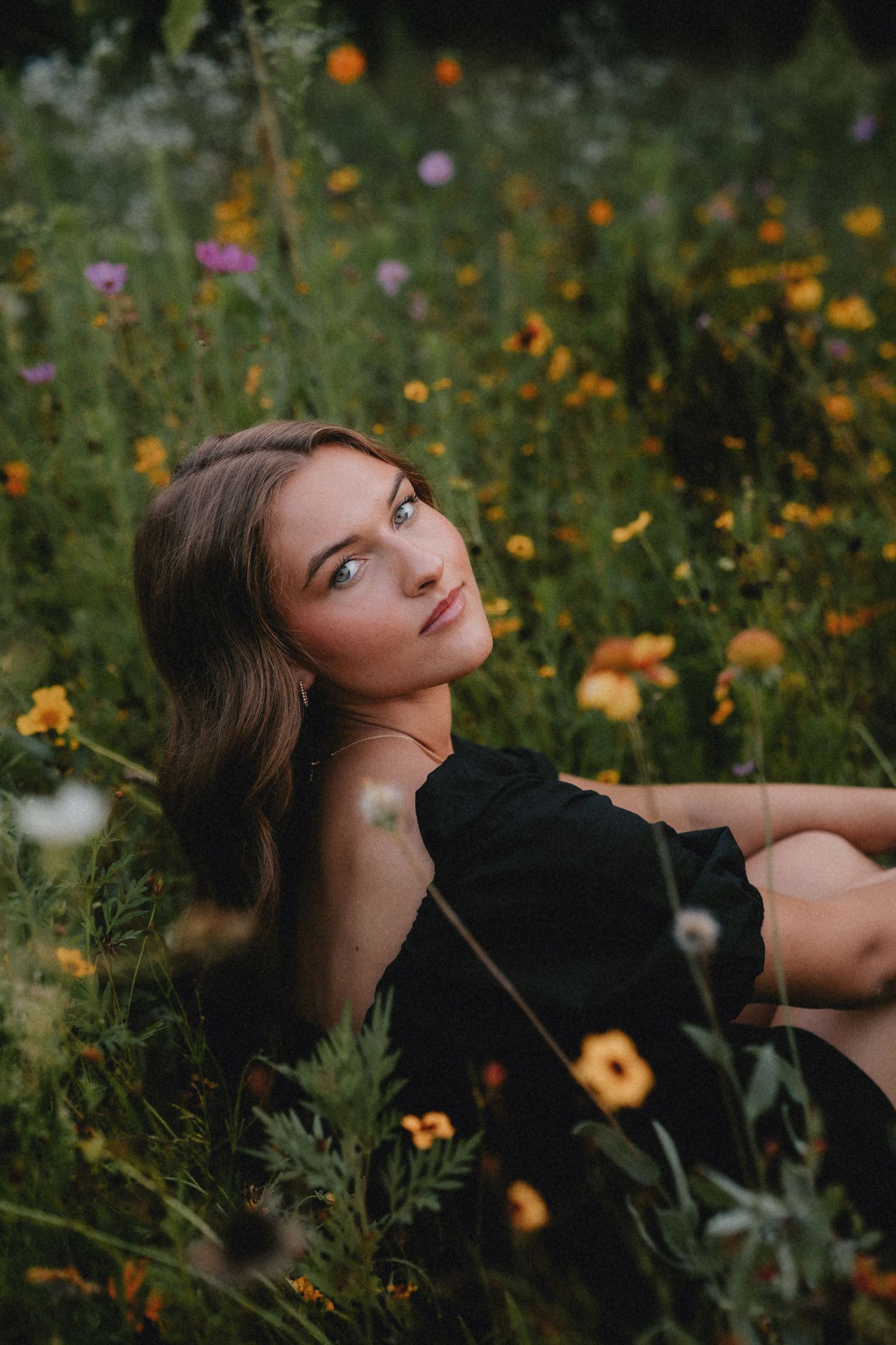 Artistic portrait in a wildflower meadow with orange and pink blooms against dark clothing.