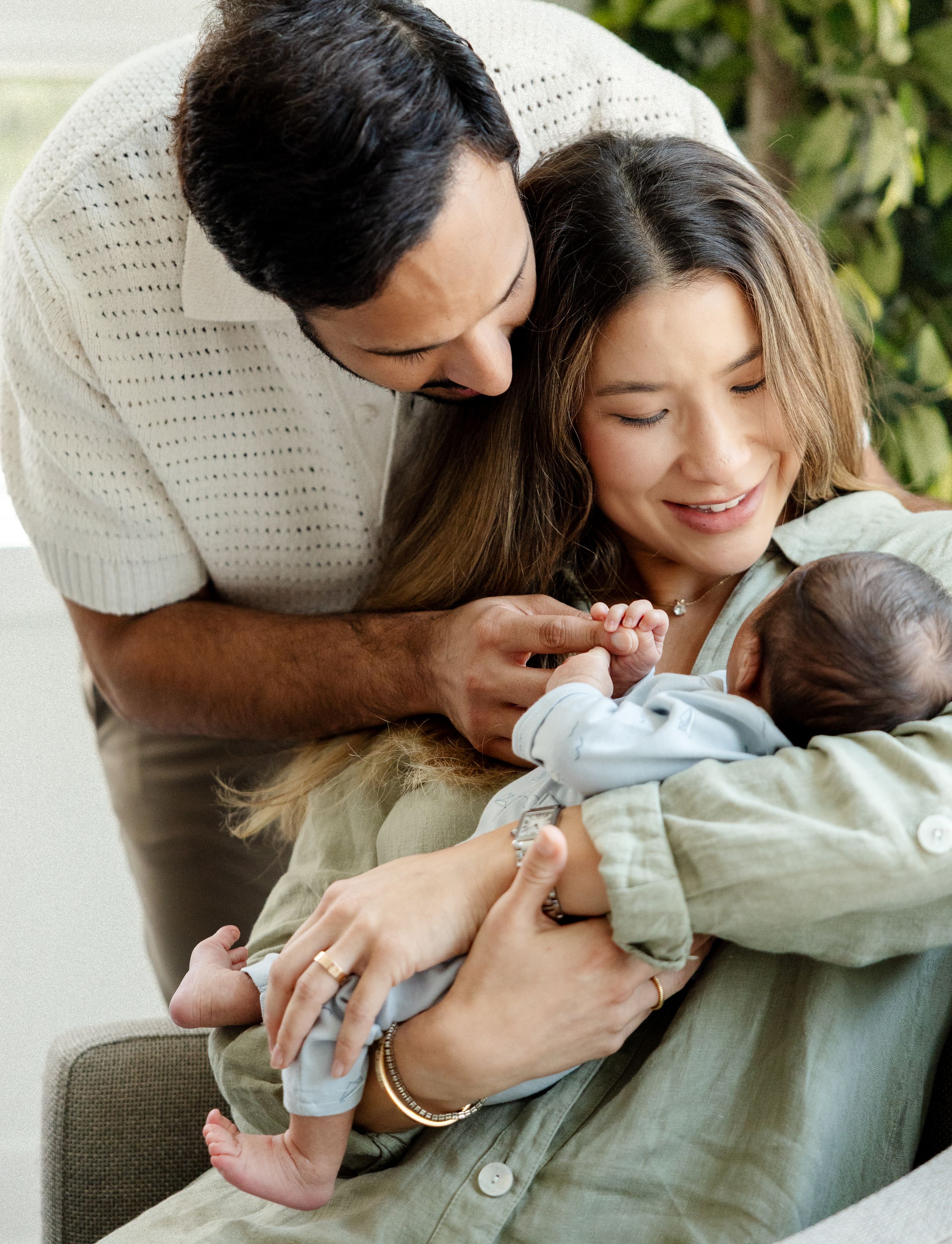 A couple shares an intimate moment with their newborn baby while relaxing on a couch at home.