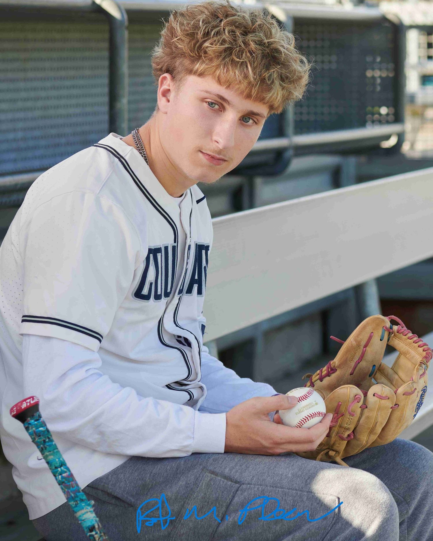 High school senior male at Heritage Recreation Center, Puyallup, sitting in dugout wearing catcher's mitt on baseball field.