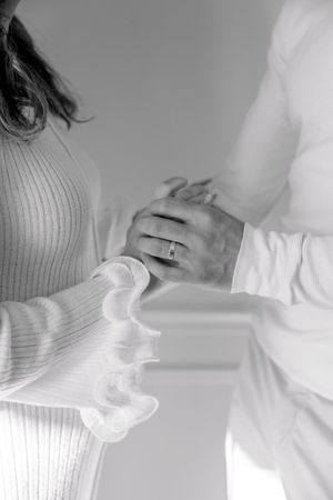A black and white close-up photo showing hands clasped together, with one person wearing a ribbed sweater and a ring.