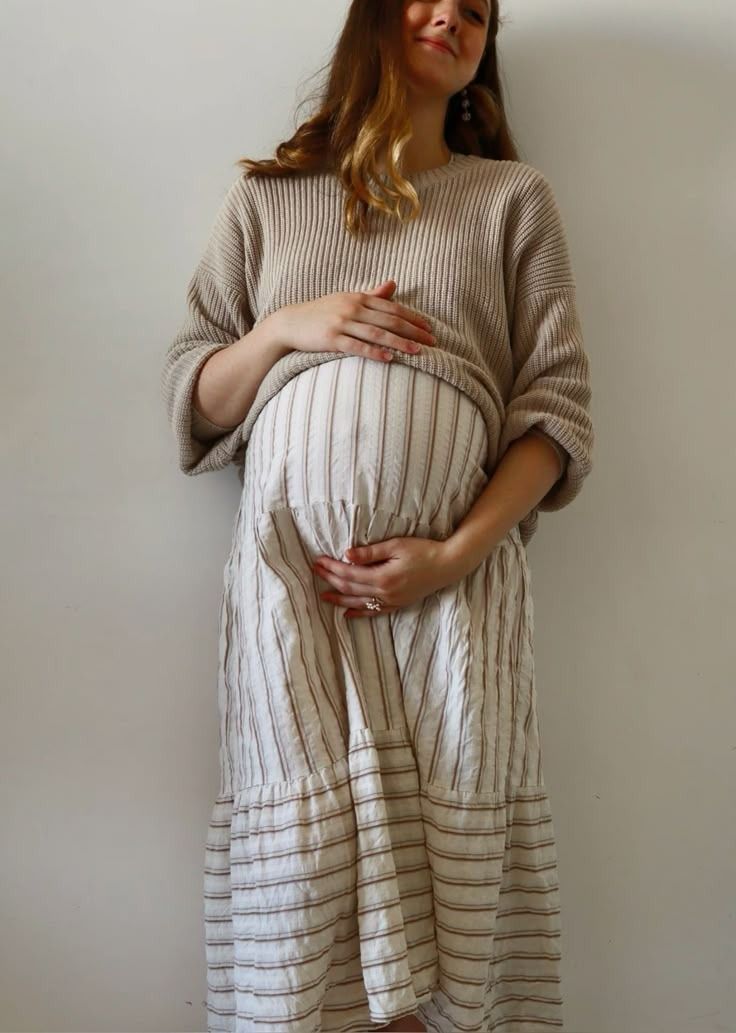 A person wearing a cozy beige sweater and striped linen apron dress shows different angles of the casual outfit.