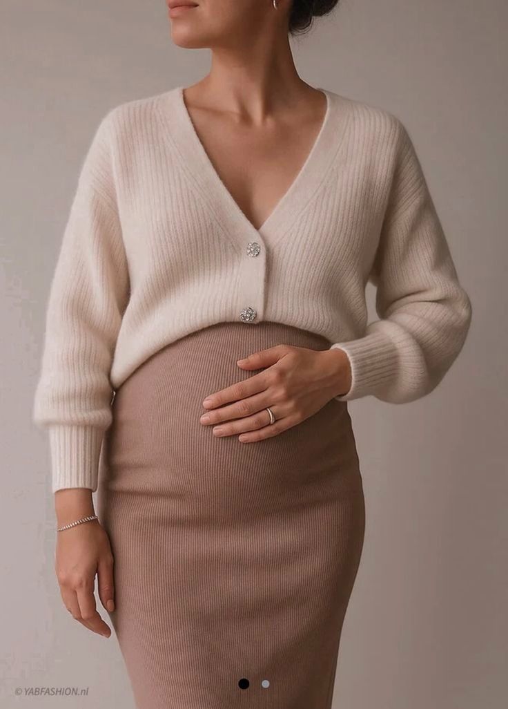 Model showcases a cream colored cropped cardigan paired with a form-fitting brown skirt in a studio setting.