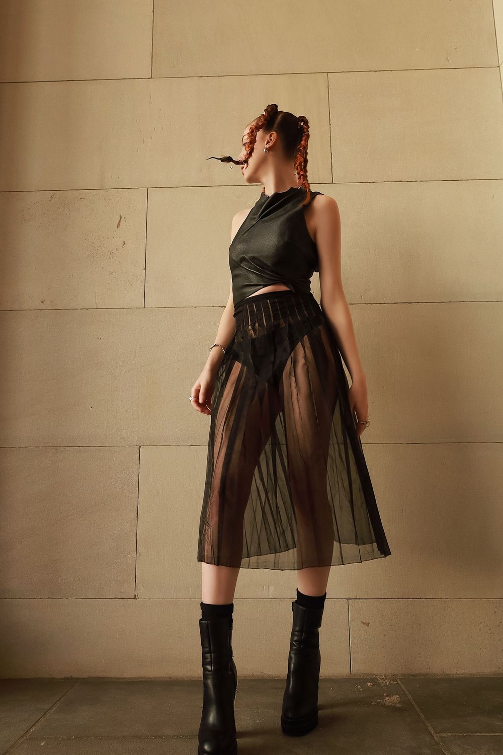 Fashion model in black crop top and sheer midi skirt poses against beige wall wearing platform combat boots.