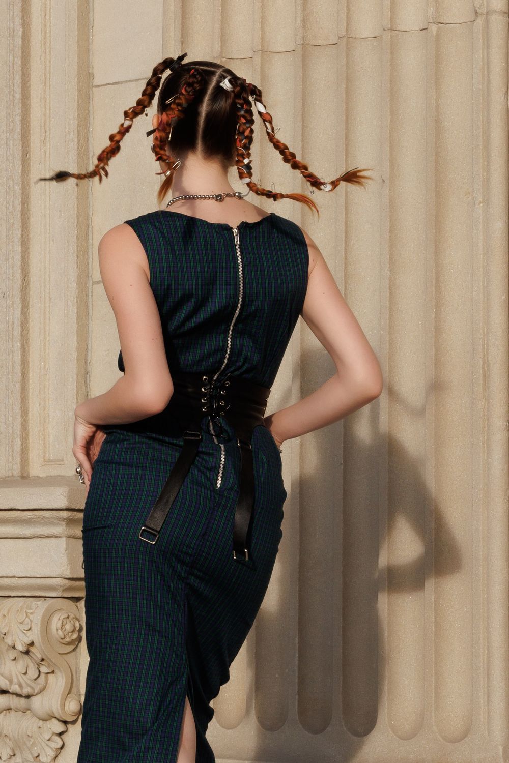 Back view of a navy pinstripe dress with corset-style lacing and braided hairstyle against a beige wall.