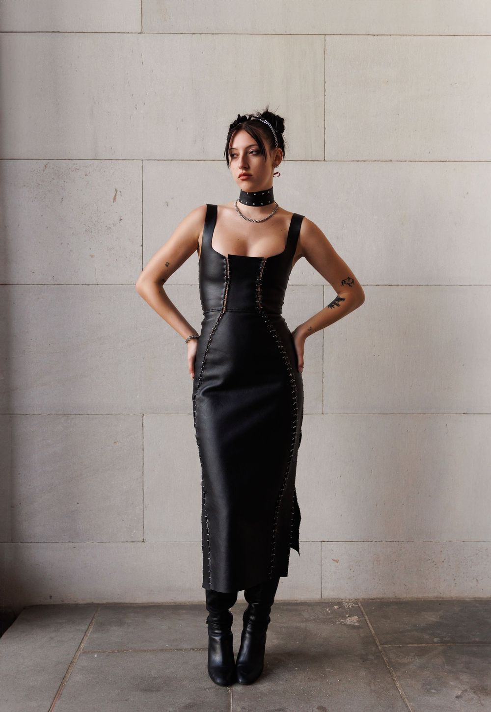 Four progressive photographs show a model in a black corset dress against a gray wall.