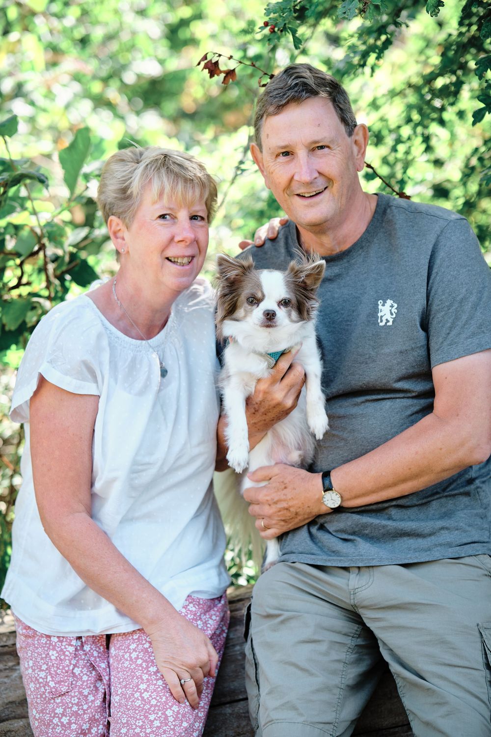 A couple sitting outdoors shares tender moments with their small brown and white dog on a sunny day.