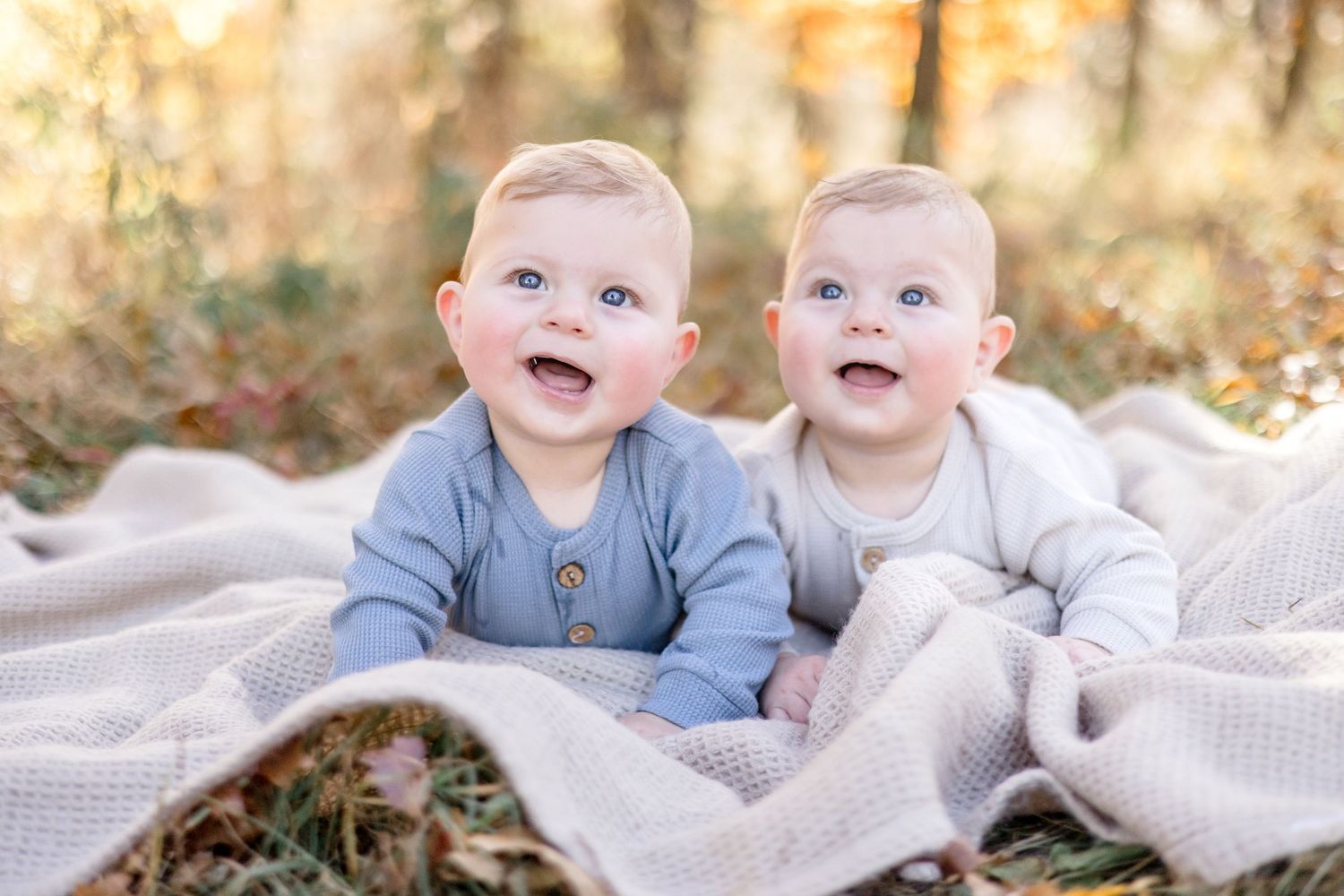 Two young children sit together on a white blanket outdoors during an autumn photoshoot.