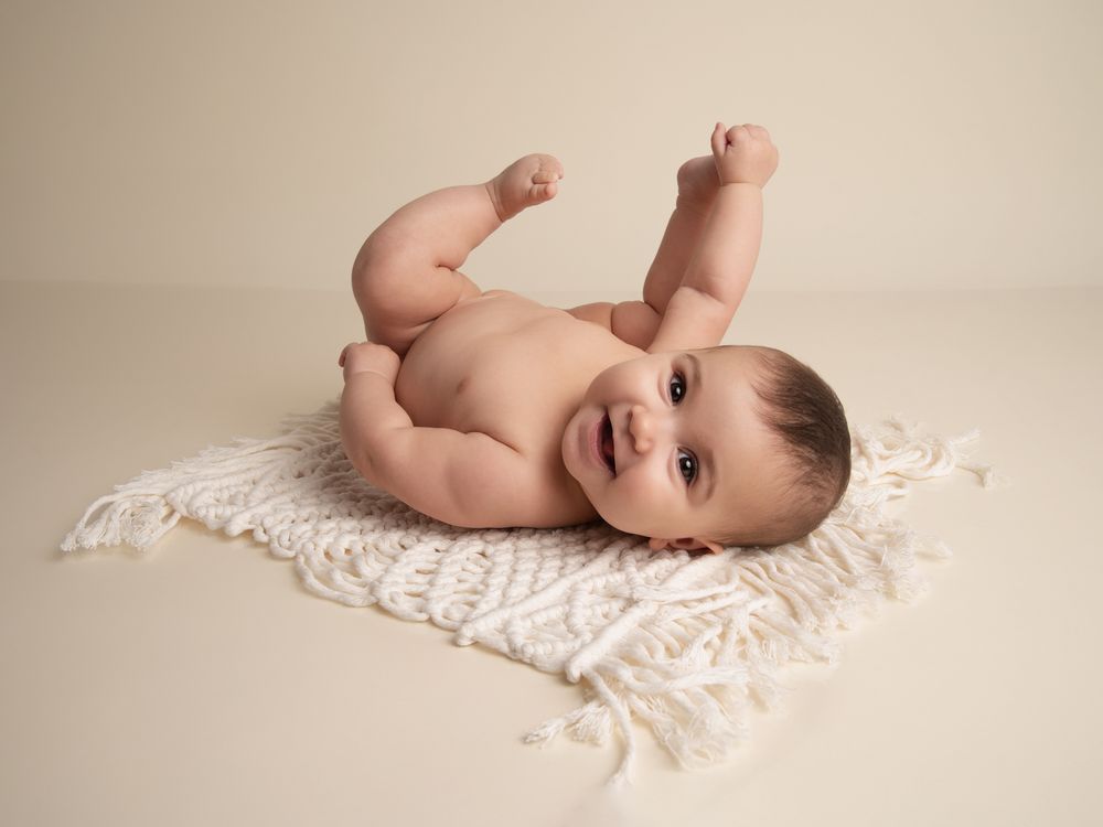 Smiling baby lying on back on white crochet blanket kicking legs up in professional studio photo.