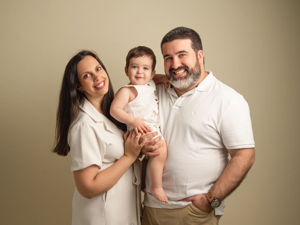Happy family portrait with mother, father, and baby girl in coordinating white outfits.