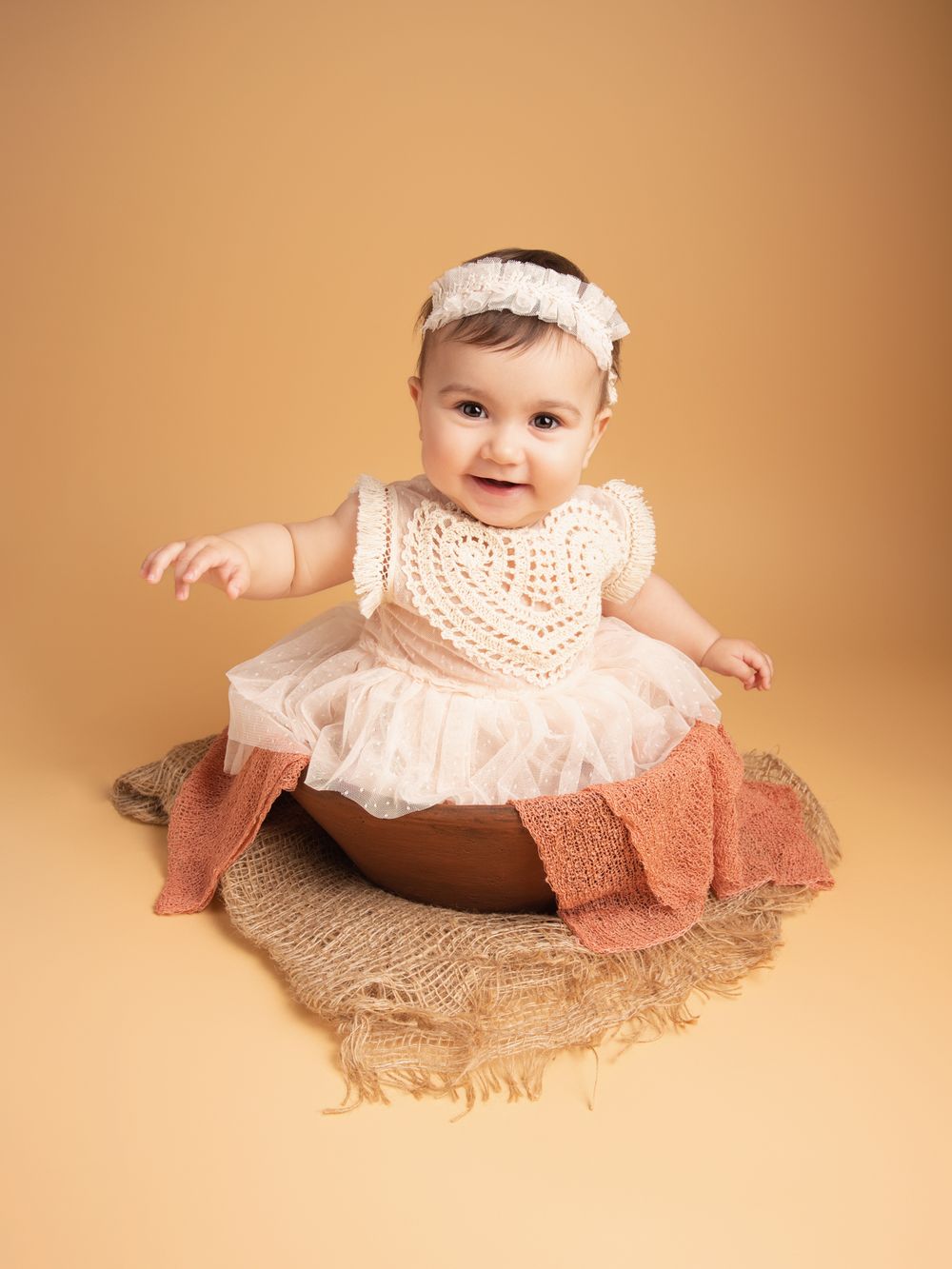 Adorable baby girl in cream tutu dress sitting in wooden bowl prop with headband in studio portrait.