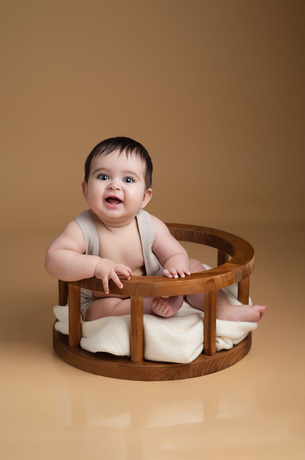 Curious baby sitting in wooden prop bed during professional milestone photography session.