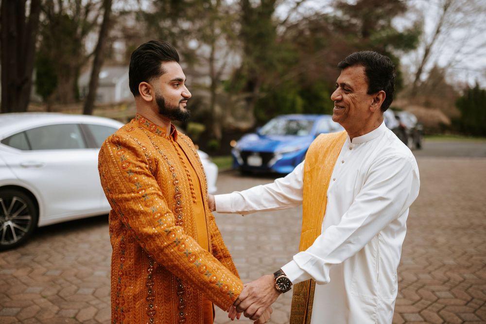 Two people in orange and white outfits greet each other warmly in an outdoor setting with cars in the background.