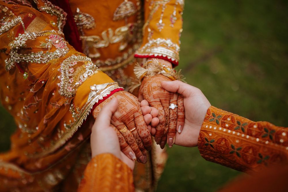Hands adorned with intricate henna designs and gold bangles hold each other in a traditional Indian wedding ceremony.