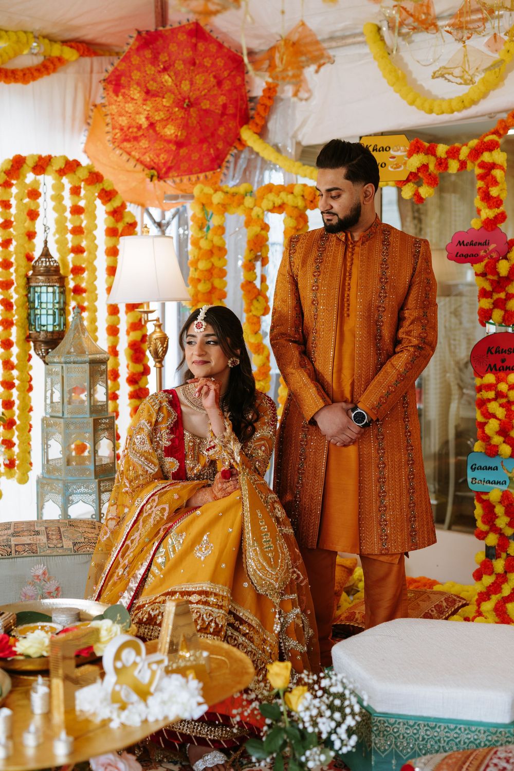 Traditional South Asian wedding ceremony with ornate orange and red decor featuring marigold garlands and hanging lanterns.