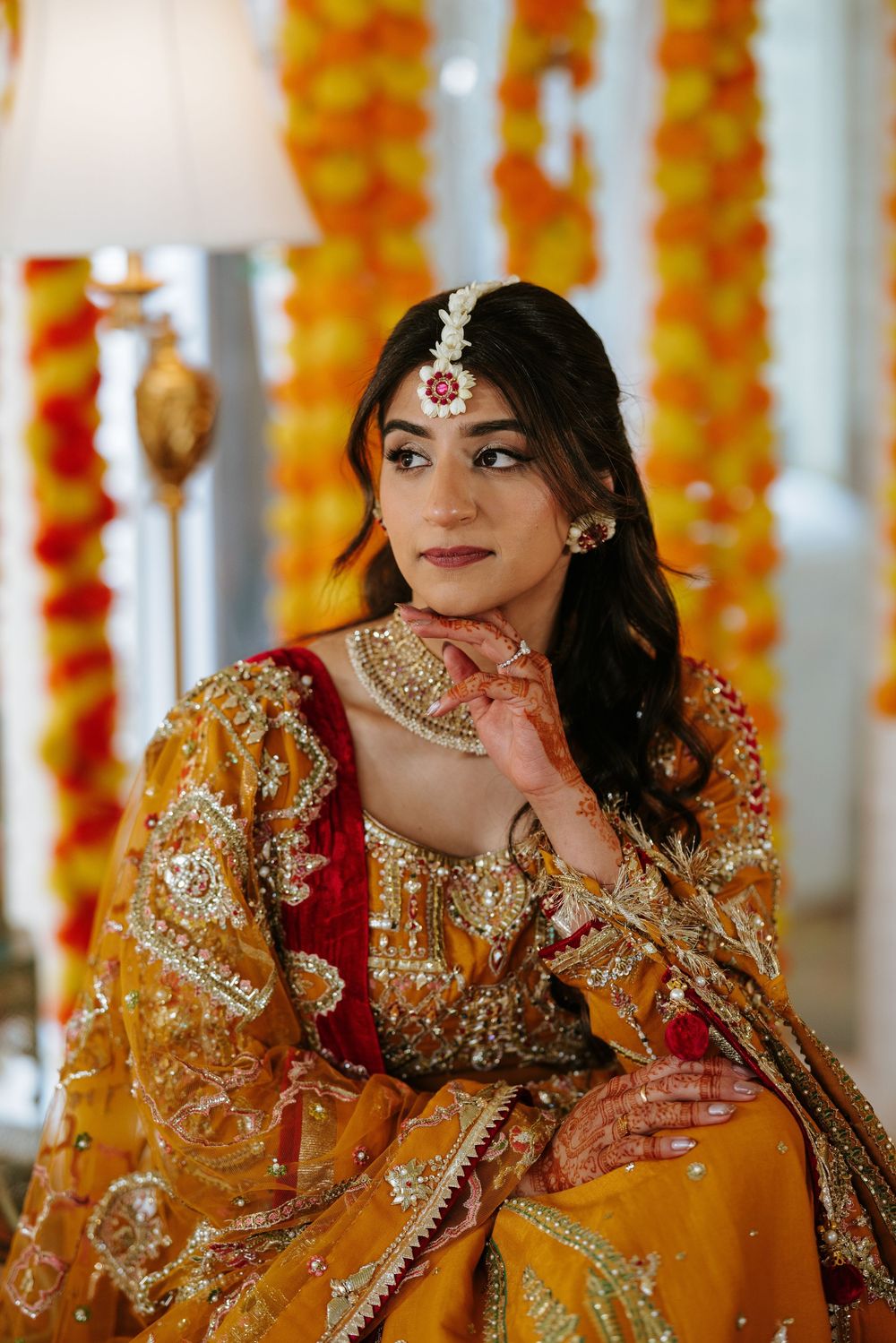 Traditional Indian bride wearing ornate red and gold embroidered attire with elegant jewelry in a marigold-decorated setting.