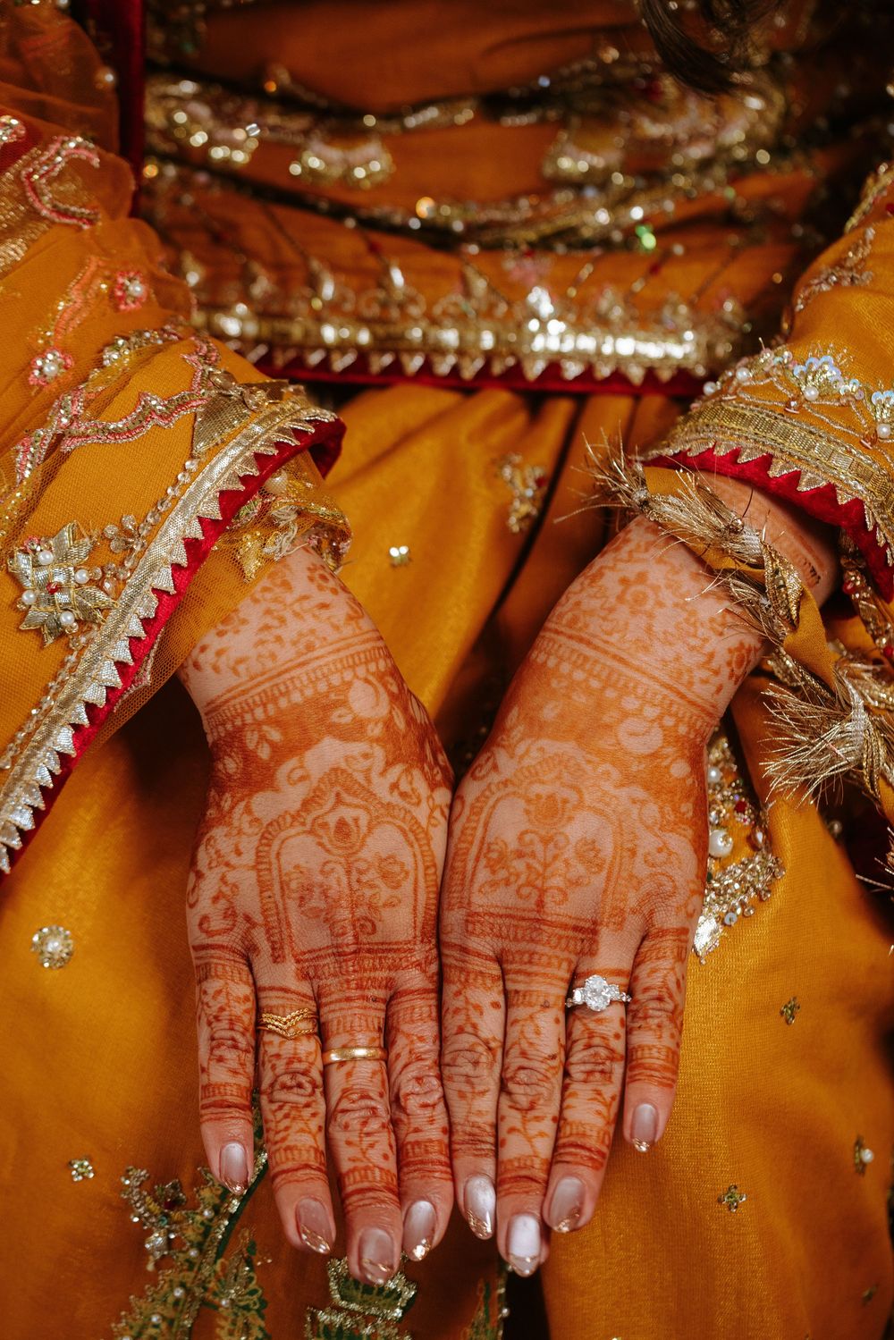 Close-up view of henna-adorned hands with traditional Indian bridal bangles and jewelry against a golden background.