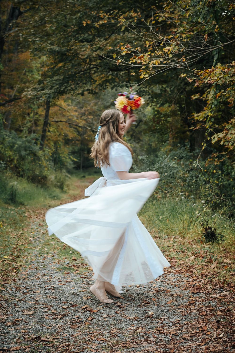 Flowing white dress twirling among autumn trees on a leaf-covered forest path.