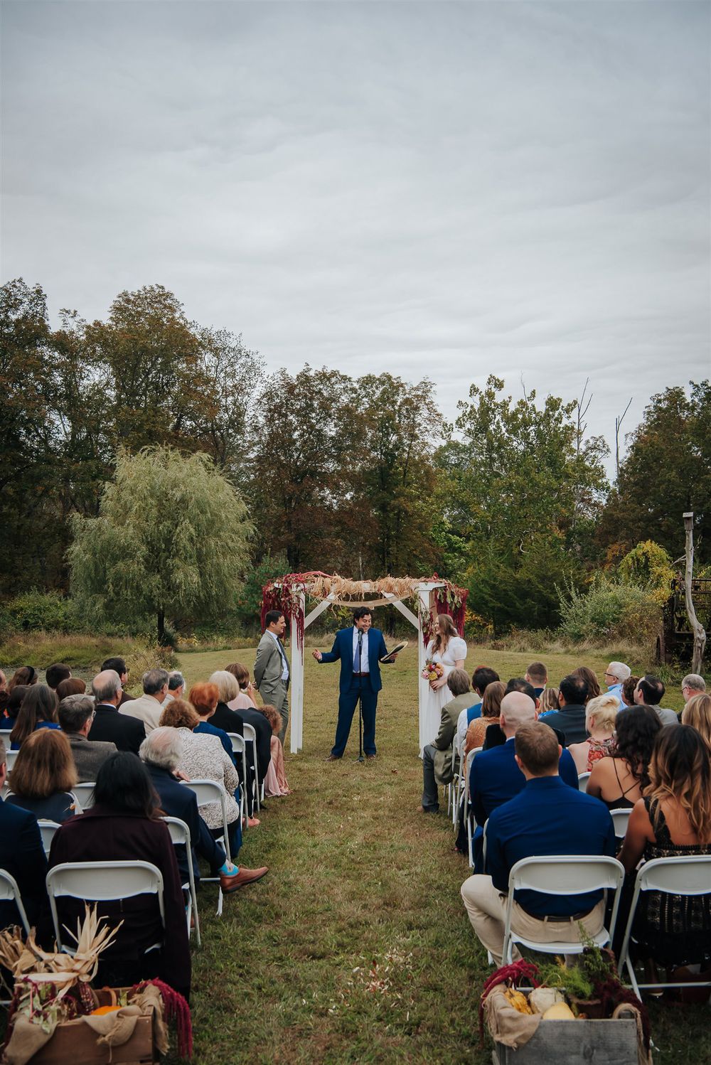 An outdoor wedding ceremony setup with rows of white chairs facing an altar area surrounded by autumn trees.
