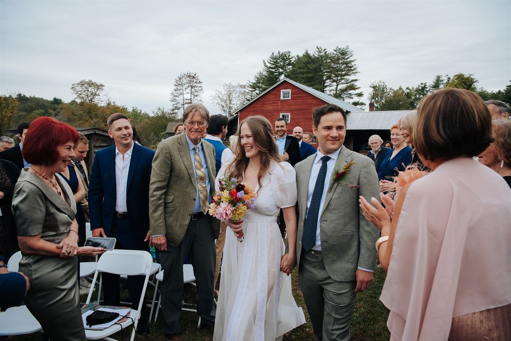 A wedding celebration at a rustic outdoor venue with guests mingling under cloudy skies.