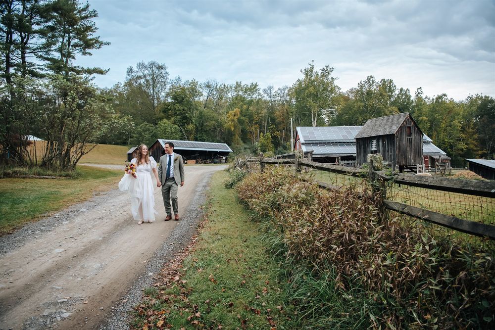 A couple walking together down a rural dirt road surrounded by autumn foliage.